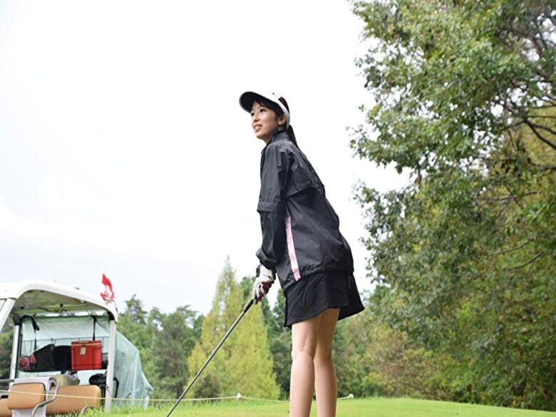 雨ゴルフでティーショットを打つゴルフ女子